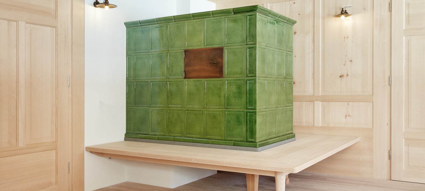 Ofenbau Voppichler – Kachelofen aus dem Bregenzerwald mit handgefertigten Geiger-Kacheln und Sandstein.