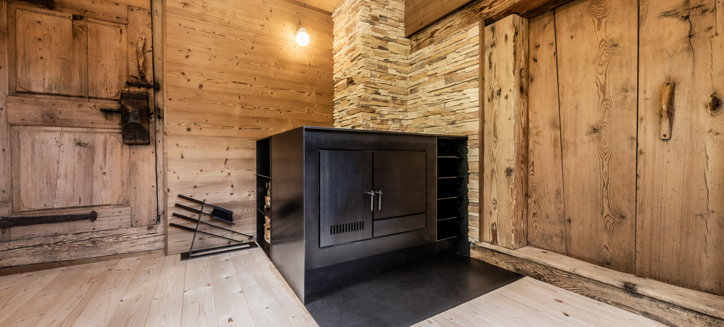 Ofenbau Voppichler – eleganter Holzofen als Durchheizherd mit Kachelspeicher, 4,3 kW und Schwarzstahl, aus dem Bregenzerwald.